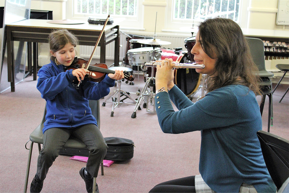Music eacher playing the flute with student playing the violin, music lessons and ensembles